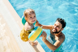little girl standing on edge of pool with her dad